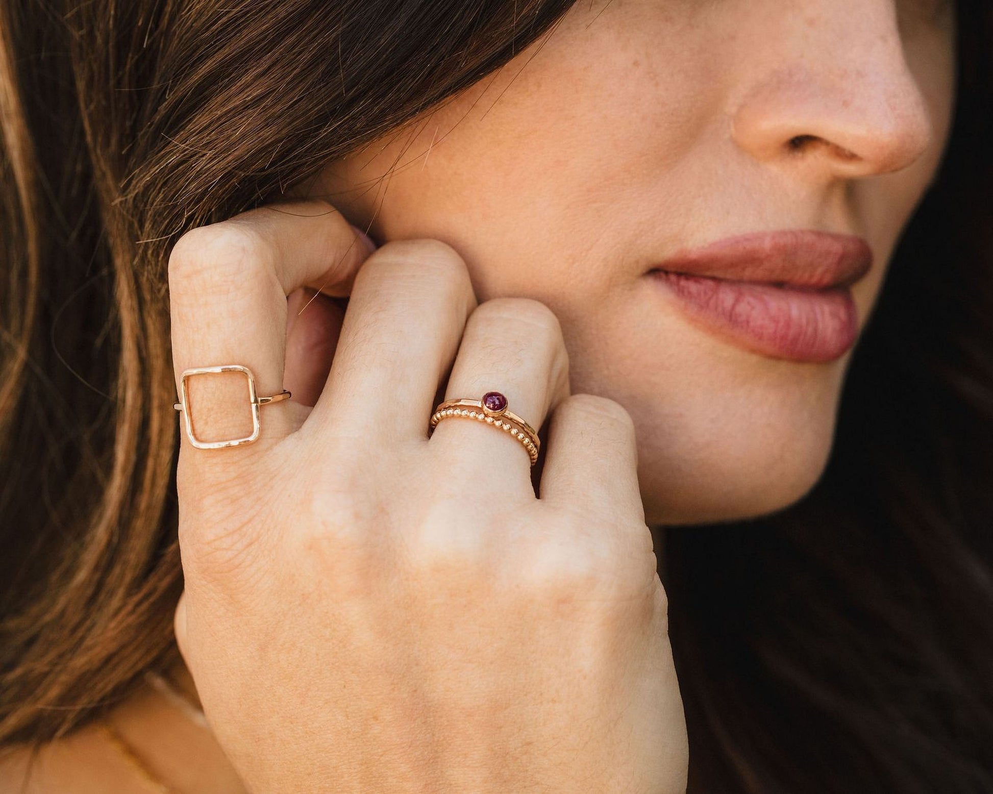 A close-up of a woman's face, focusing on her hand adorned with multiple rings.