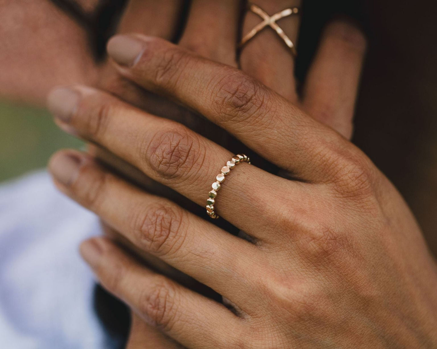 A close-up image of a person's hand wearing a gold ring with a row of small diamonds.