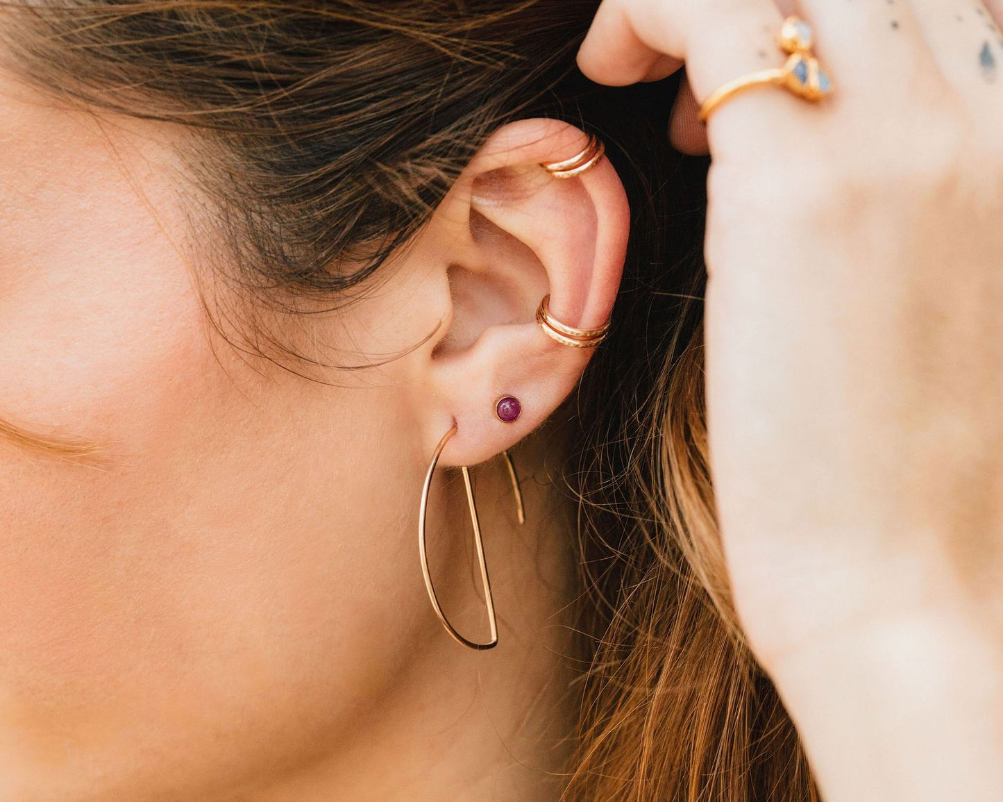 A close-up of a person's ear adorned with multiple gold earrings, including a large hoop earring and a small gemstone earring.