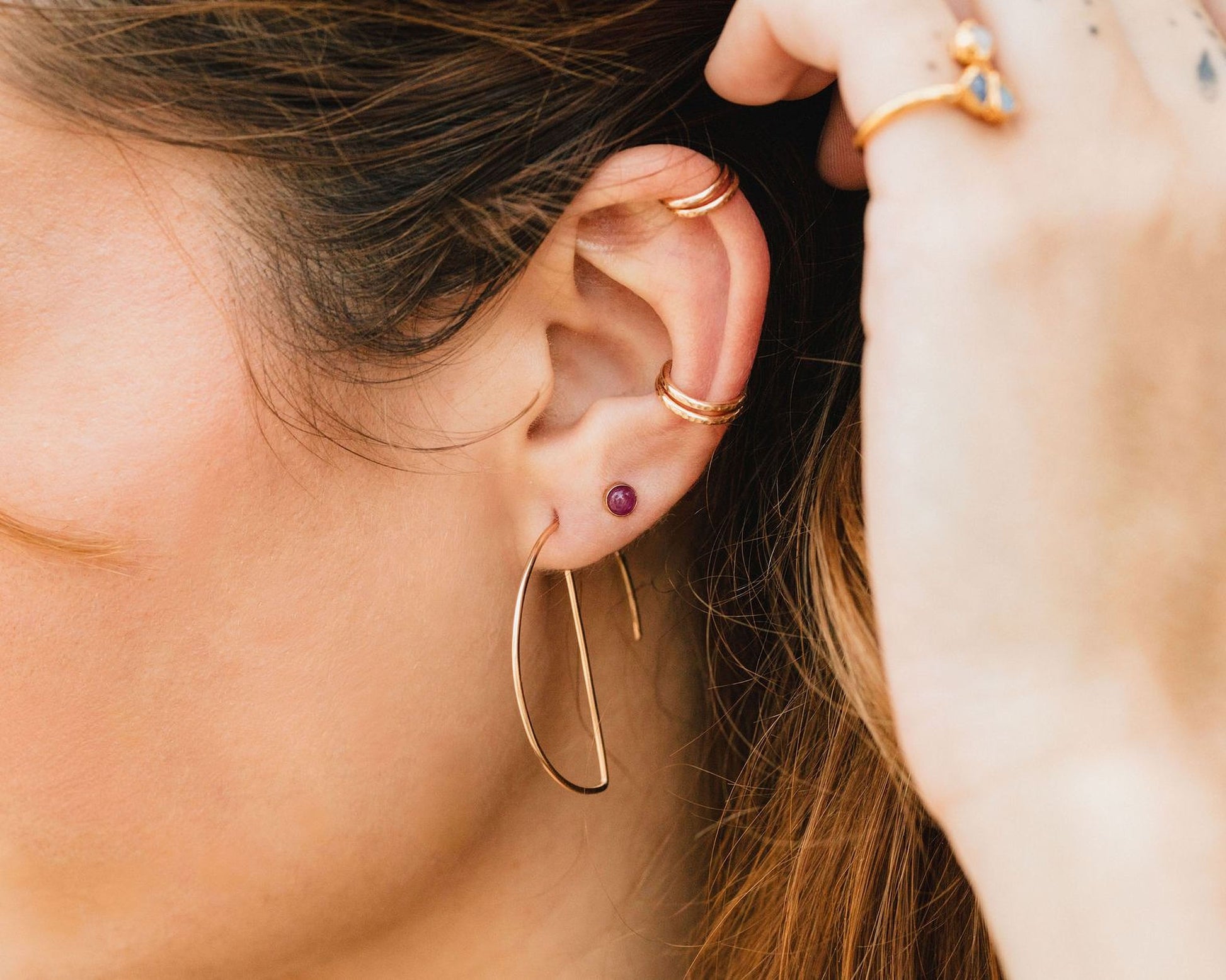A close-up of a person's ear adorned with multiple gold earrings, including a large hoop earring and a small gemstone earring.