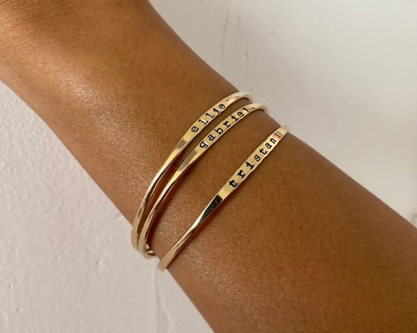 A gold-colored bracelet with engraved names on it, worn on a person's wrist.