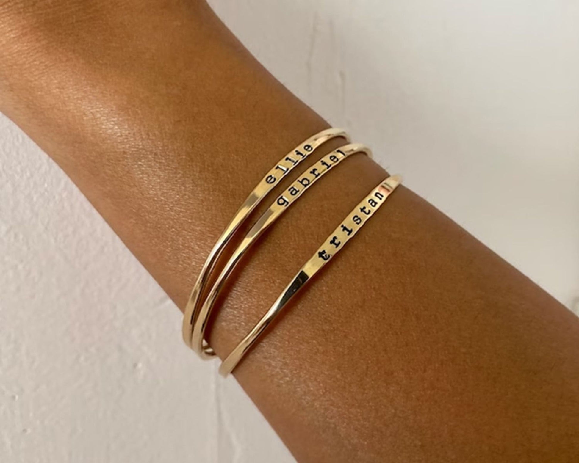 A gold-colored bracelet with engraved names on it, worn on a person's wrist.
