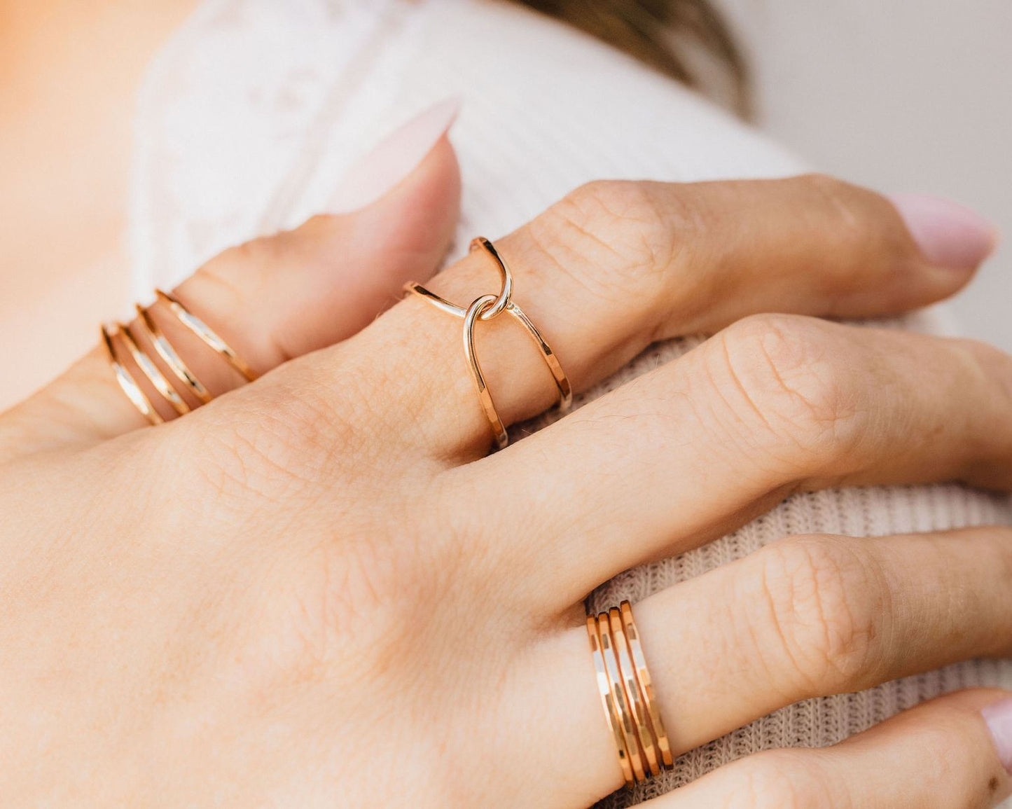 A close-up view of a person's hand wearing multiple gold rings on different fingers.