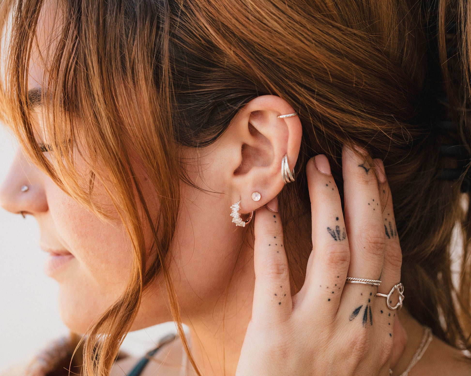 A close-up of a person's face, focusing on their earrings and tattoos.