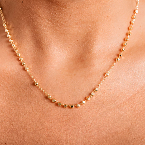 A close-up view of a delicate gold necklace with small, round beads strung together.