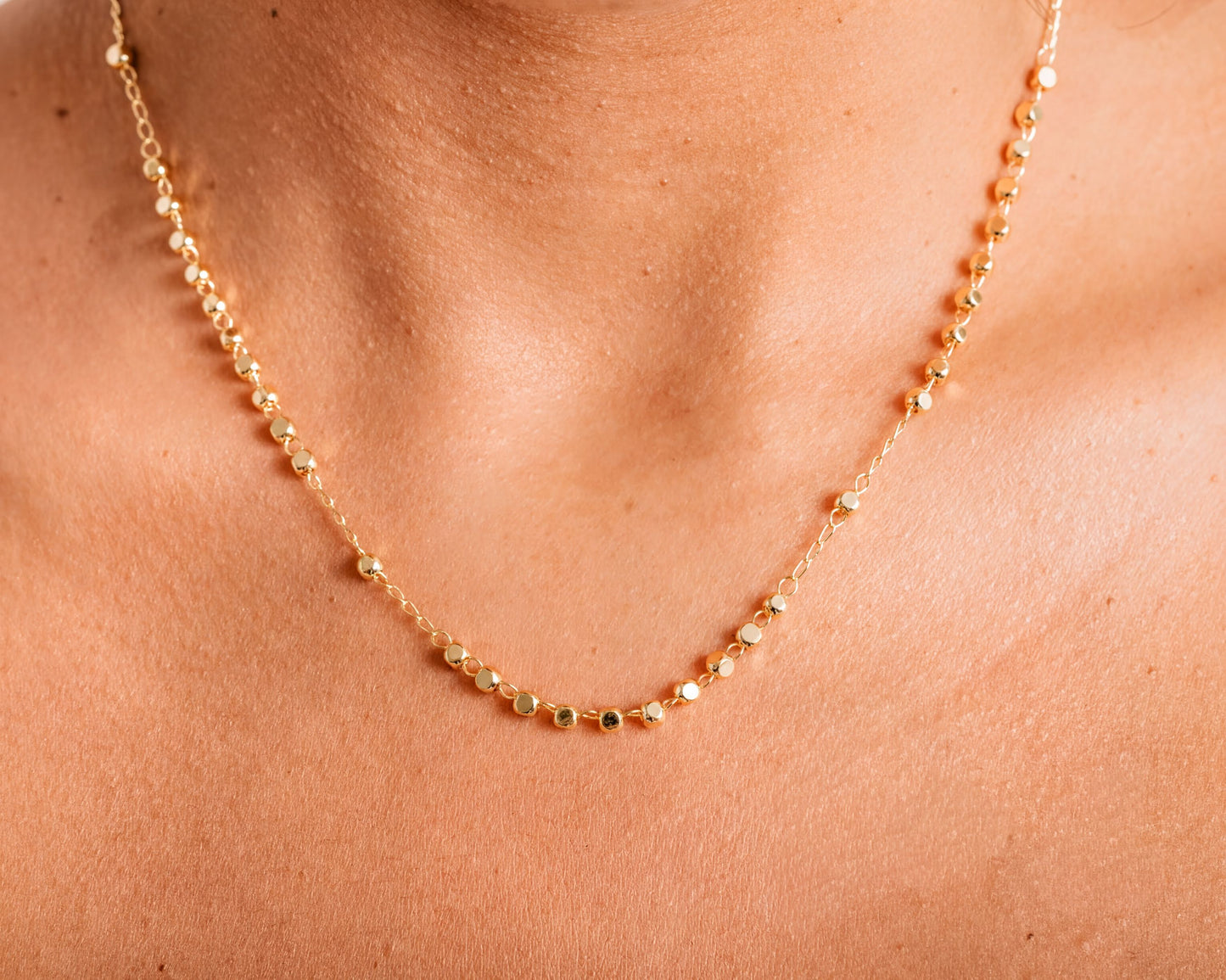 A close-up view of a delicate gold necklace with small, round beads strung together.