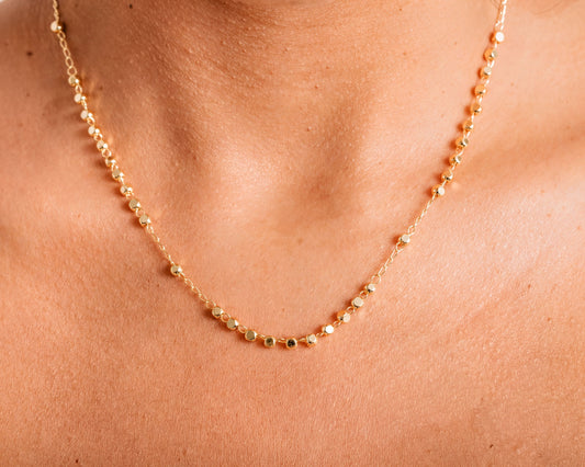 A close-up view of a delicate gold necklace with small, round beads strung together.