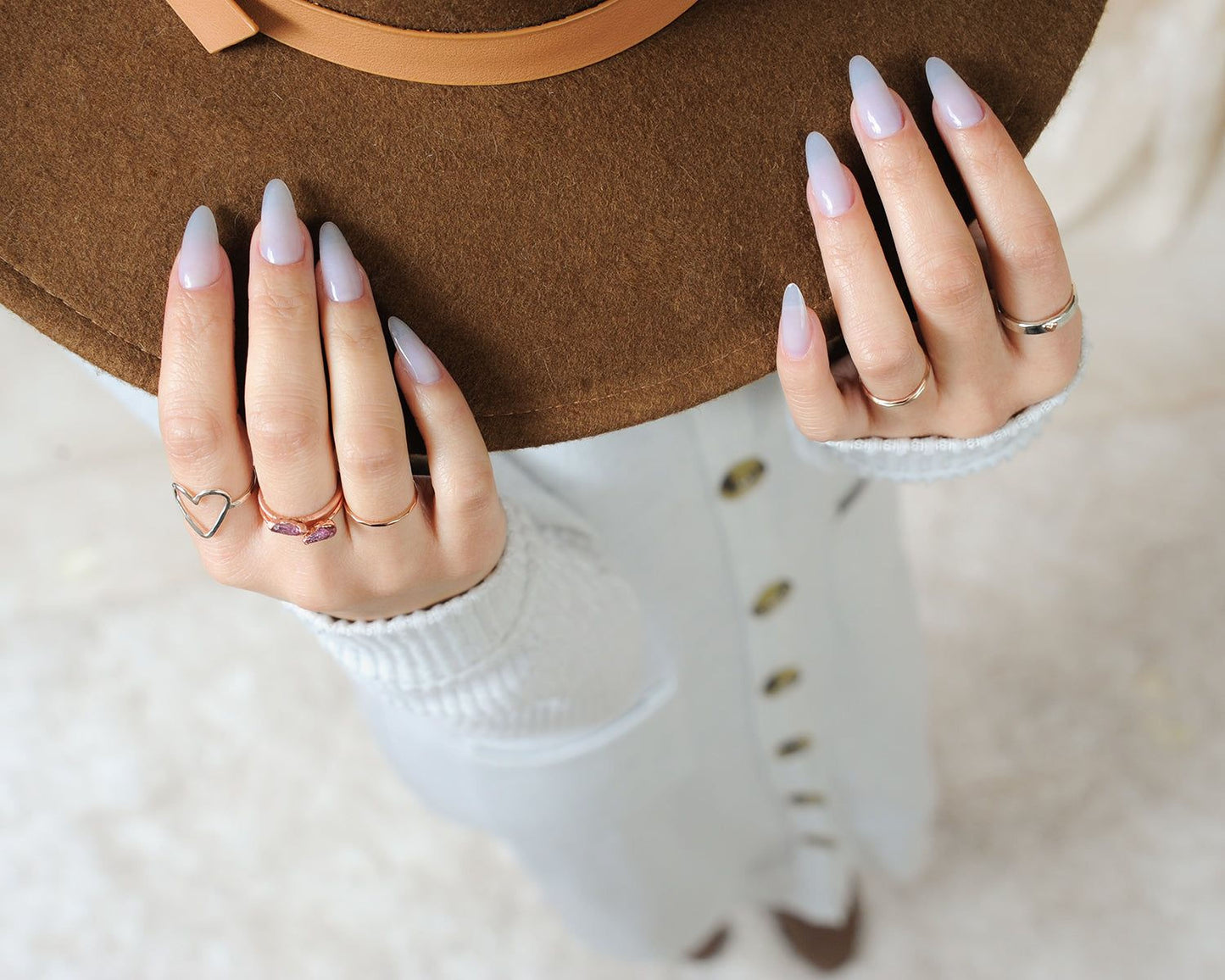 A close-up view of a person's hands wearing multiple rings, with their nails painted in a light color.