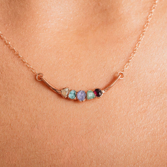 A close-up of a delicate gold necklace with a row of colorful gemstones on the pendant.