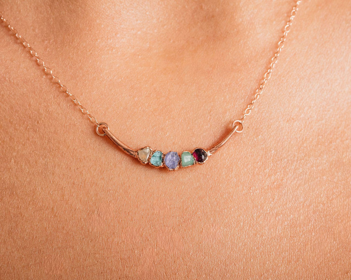 A close-up of a delicate gold necklace with a row of colorful gemstones on the pendant.