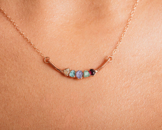 A close-up of a delicate gold necklace with a row of colorful gemstones on the pendant.