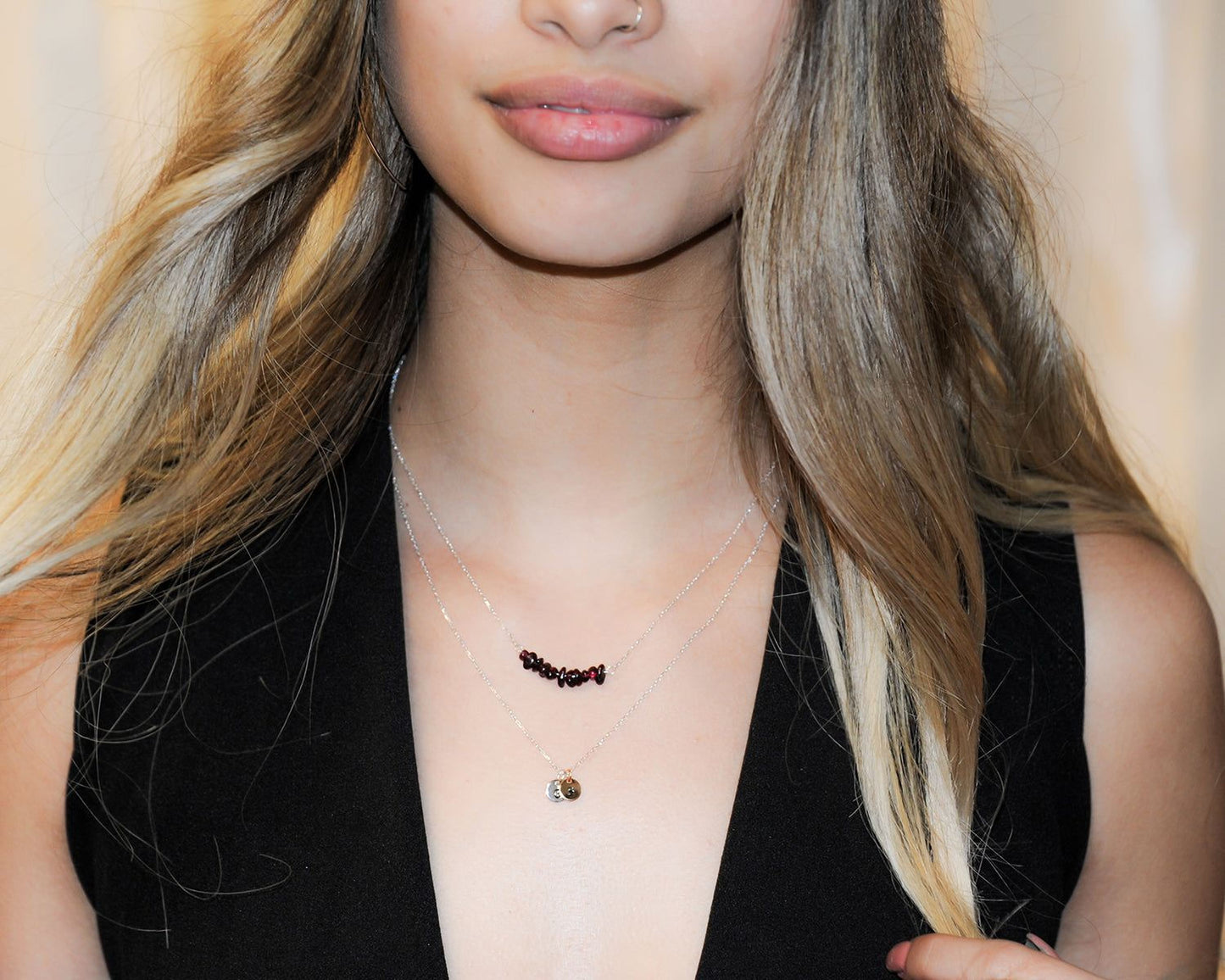 A close-up of a woman's face wearing a necklace with a pendant and a small charm.