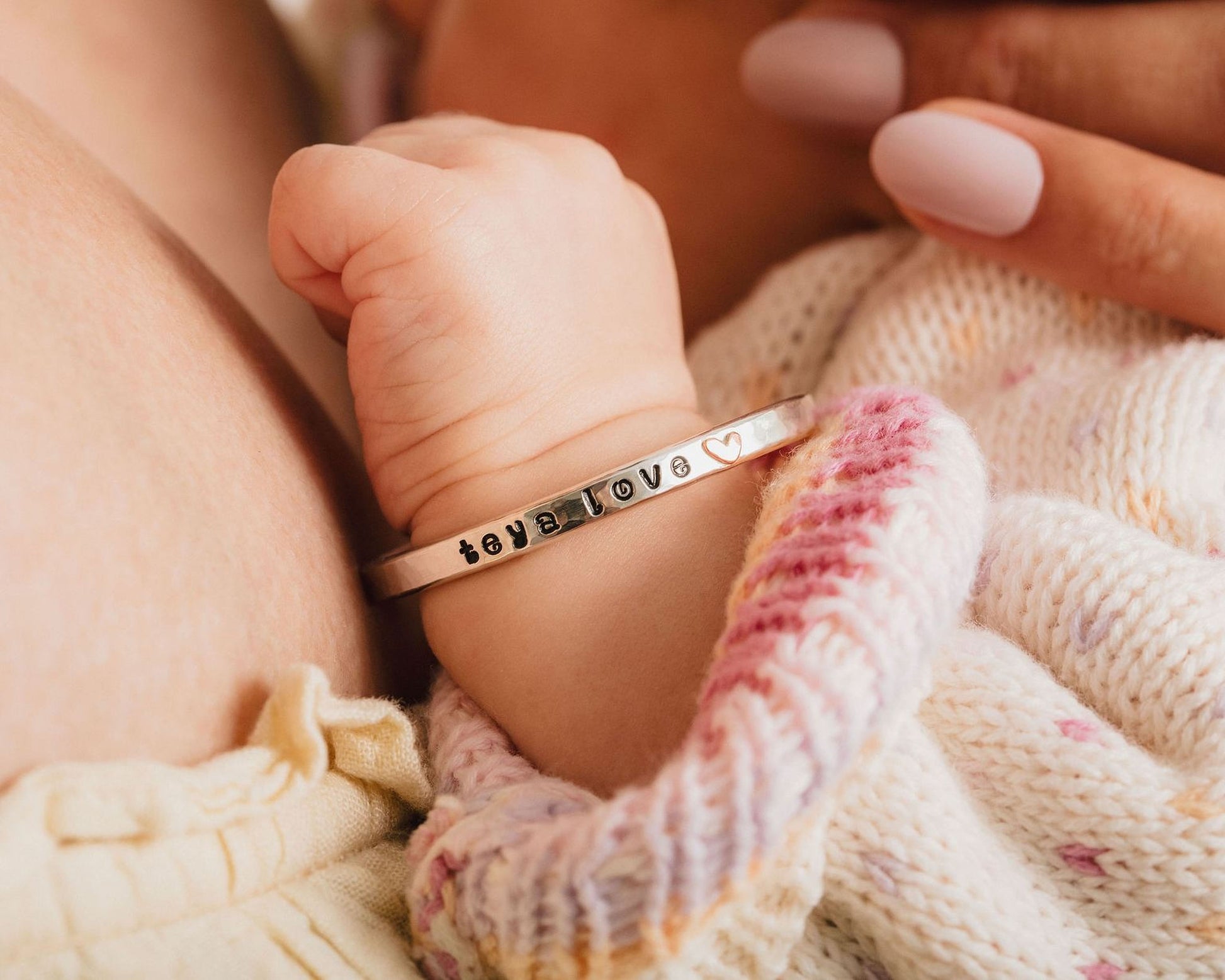 A close-up image of a baby's hand wearing a bracelet with the word "love" engraved on it.