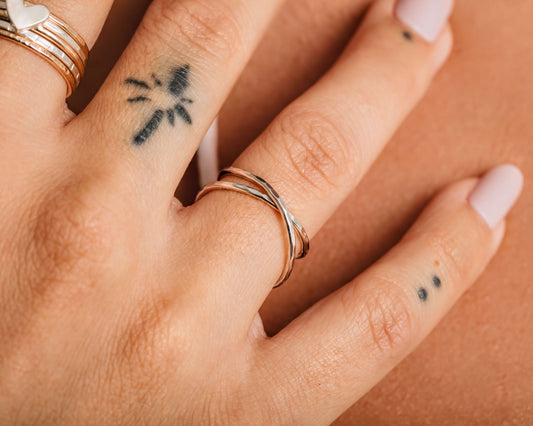 A close-up of a person's hand wearing a ring and having a tattoo on one of the fingers.