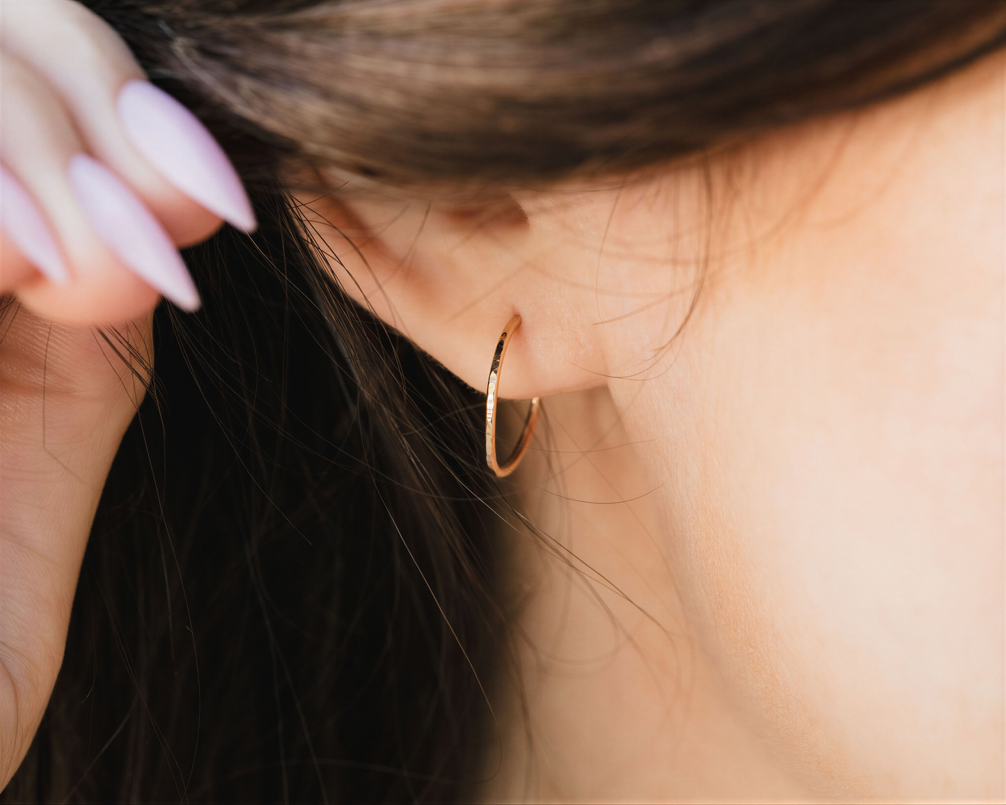 A close-up view of a person's ear with a gold hoop earring, with their hair visible in the background.