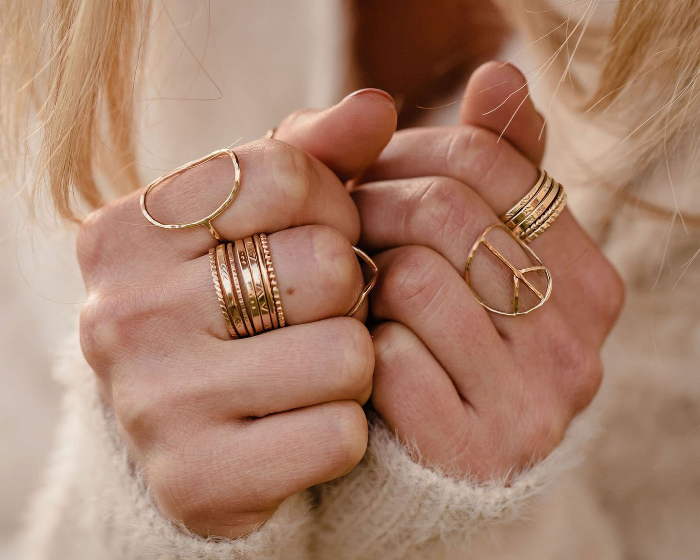 A close-up image of a person's hands wearing multiple gold rings on their fingers.