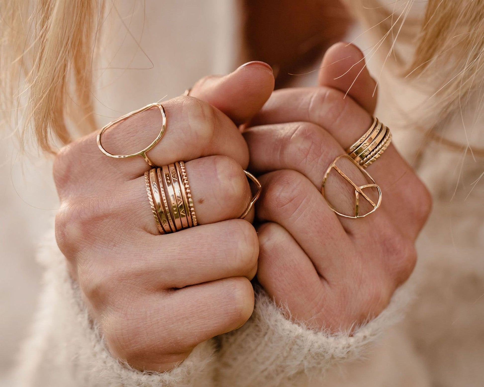 A close-up image of a person's hands wearing multiple gold rings on their fingers.