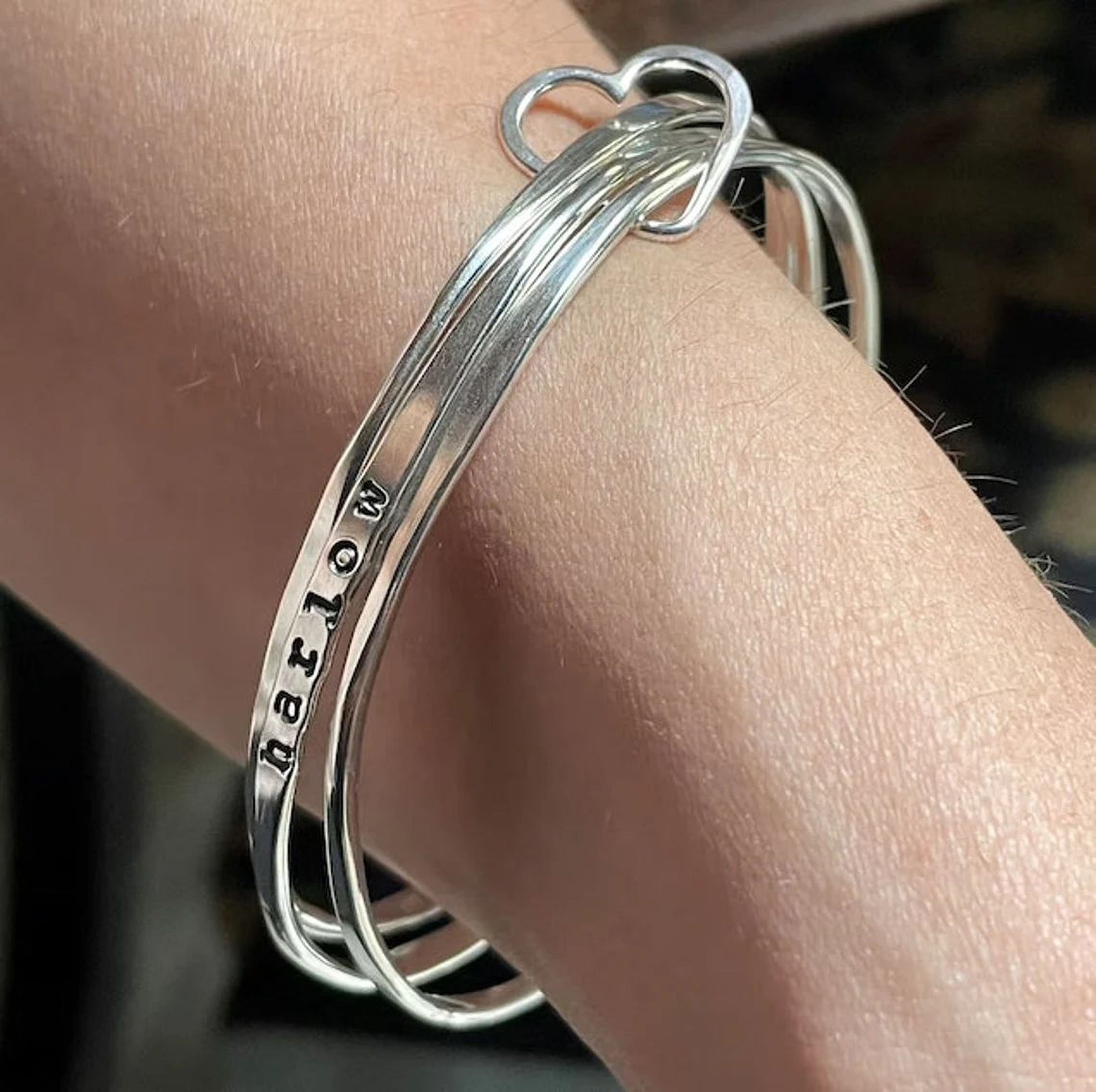 A silver bracelet with a heart-shaped charm attached to it, worn on a person's wrist.