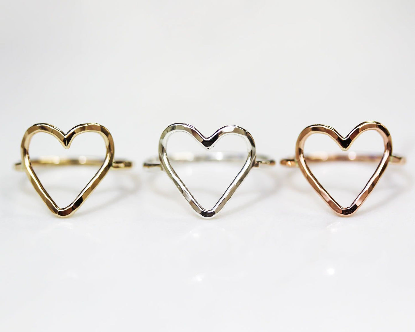 Three heart-shaped rings are displayed in a row, each with a unique color and design.