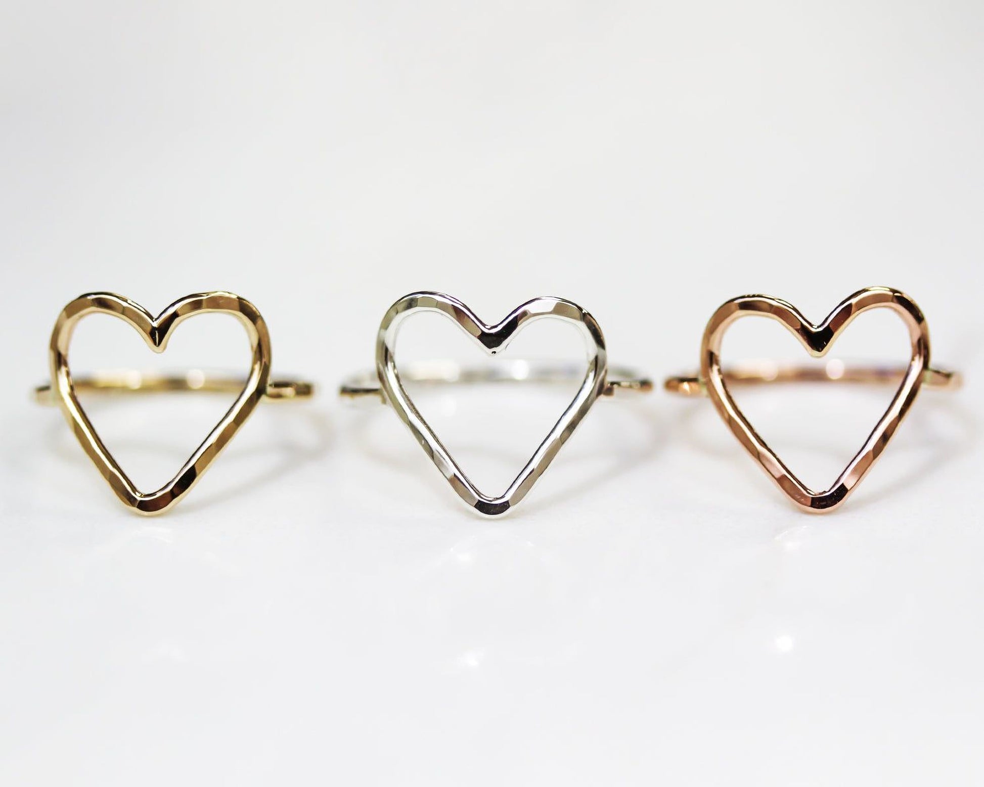 Three heart-shaped rings are displayed in a row, each with a unique color and design.