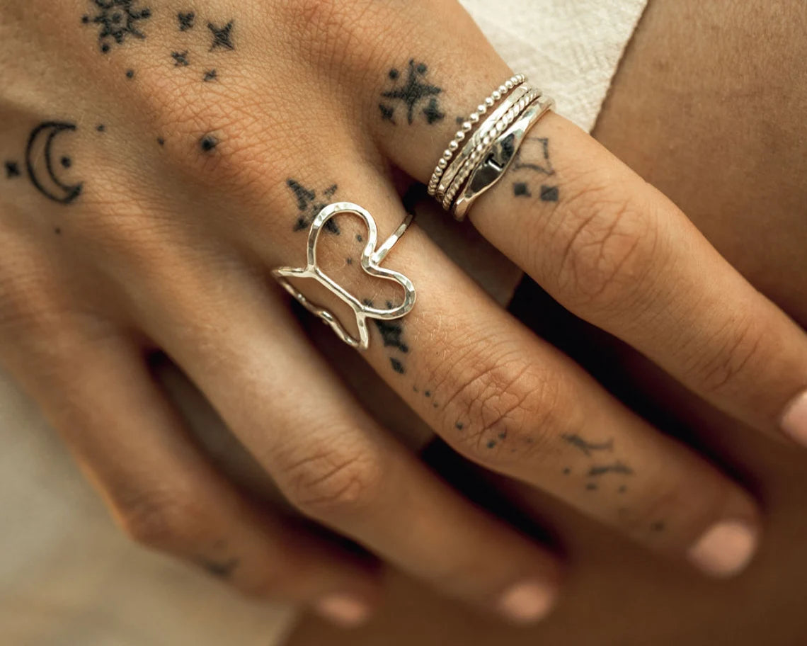A close-up of a person's hand adorned with multiple rings and tattoos on the fingers.
