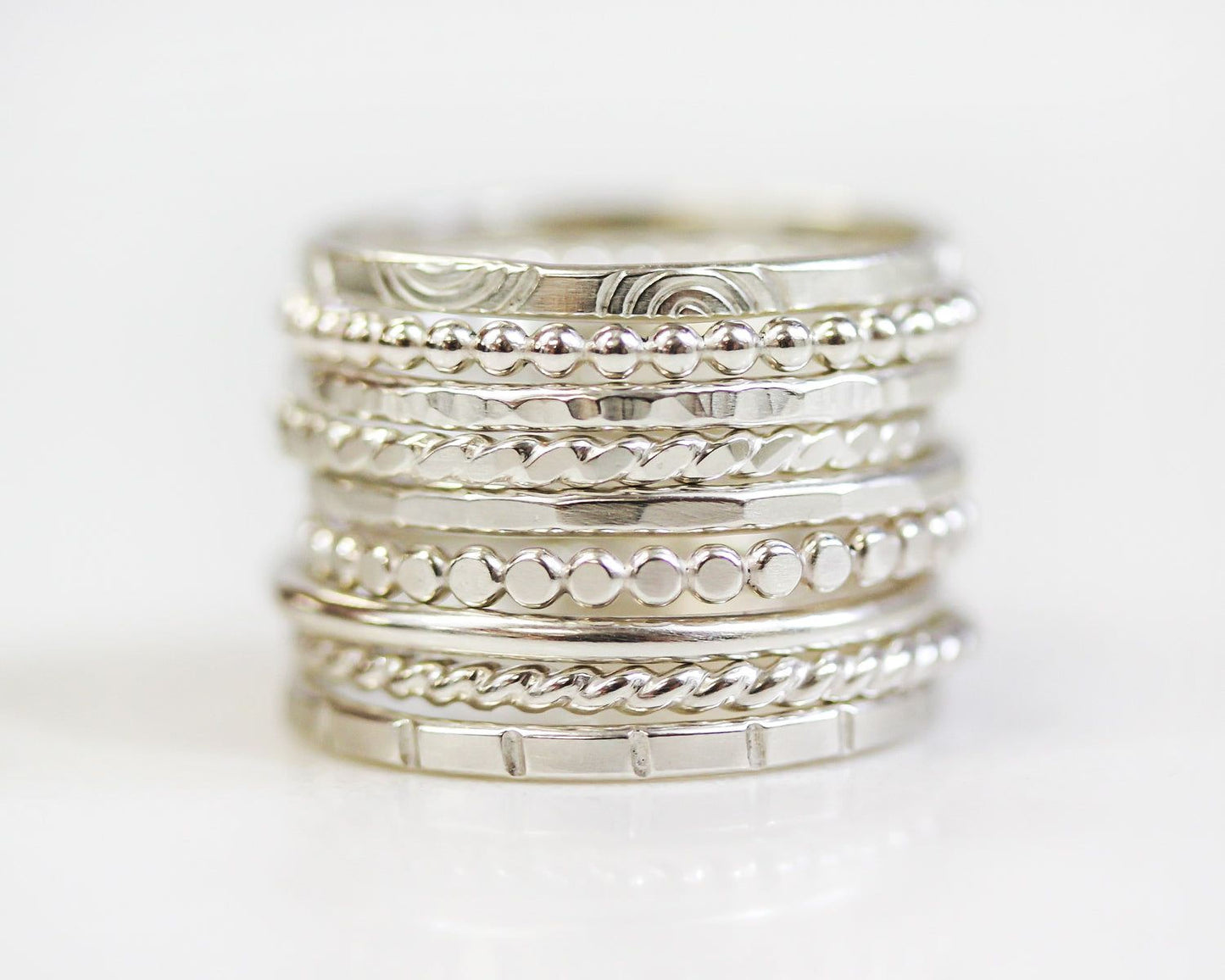 A stack of silver rings with various designs and textures.