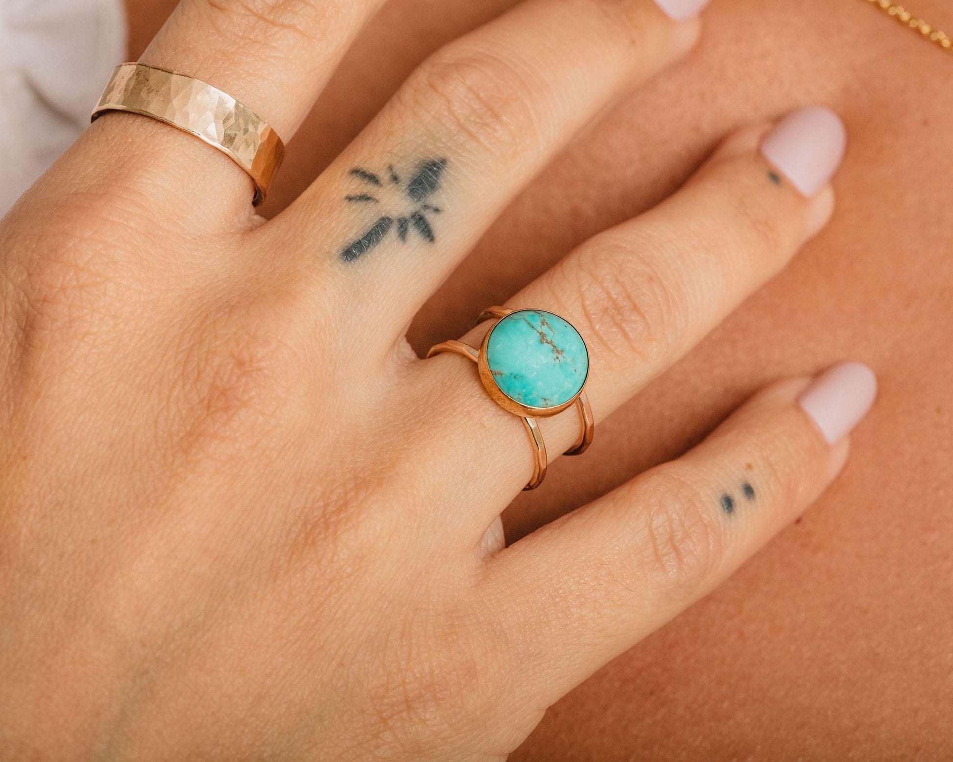 A close-up of a person's hand wearing a turquoise stone ring and a gold ring on the same finger.