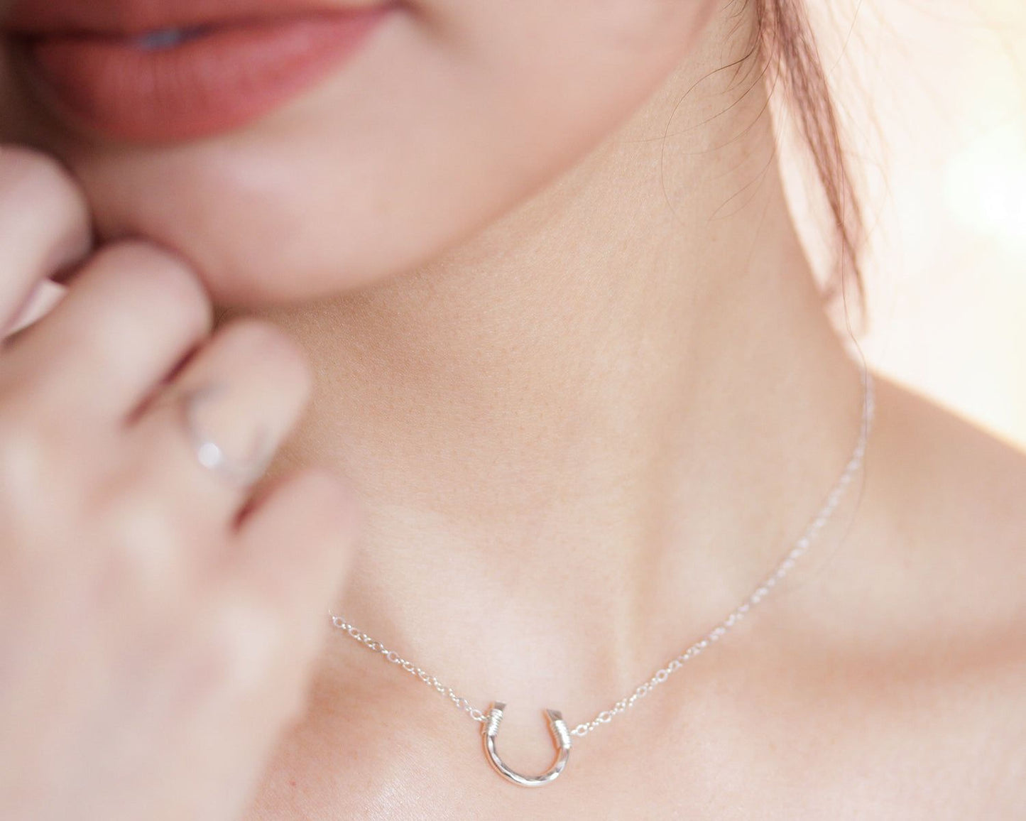 A close-up of a person's face, focusing on their hand and the delicate chain necklace they are wearing.
