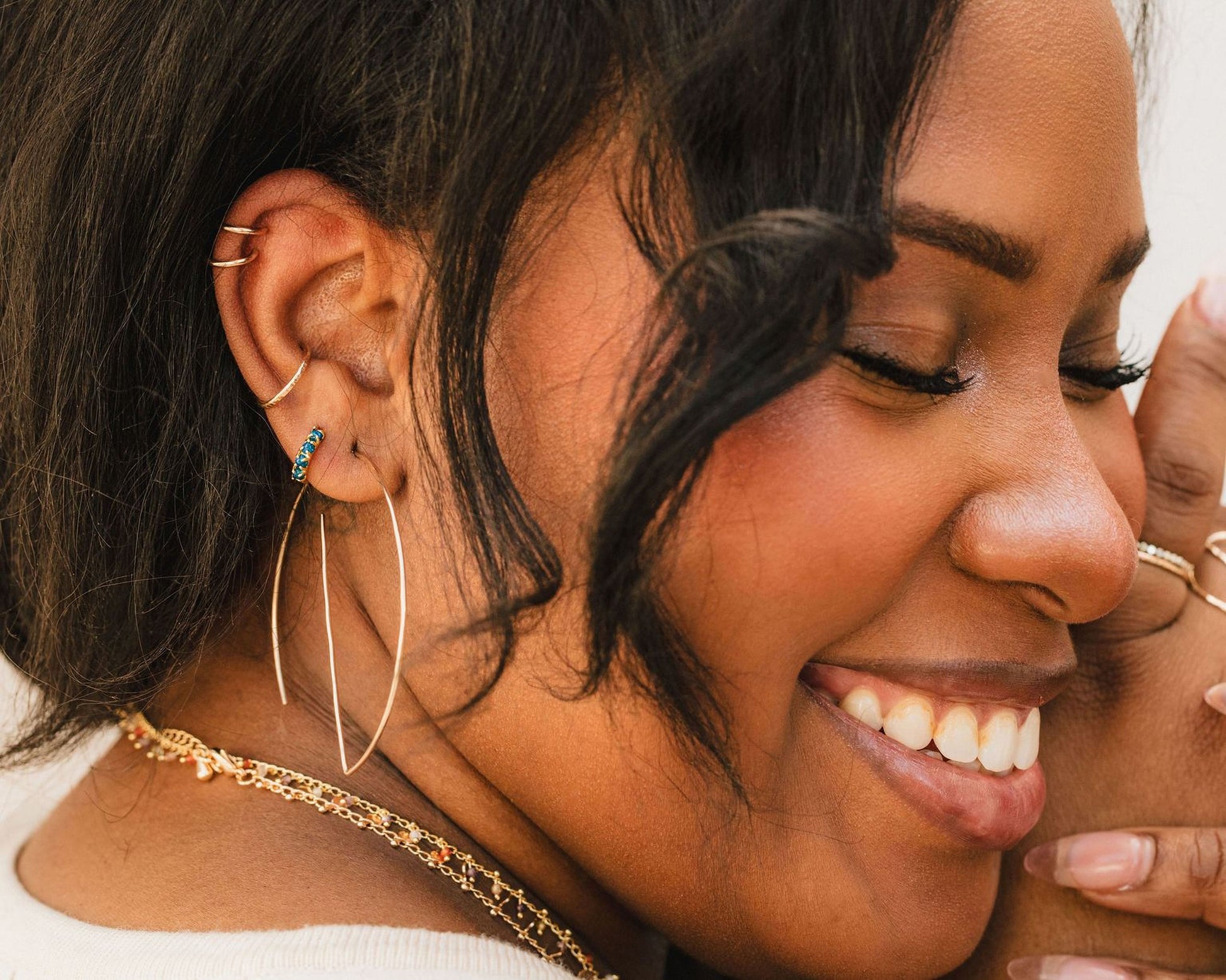 A close-up of a smiling woman with dark hair and multiple earrings, wearing a white top.