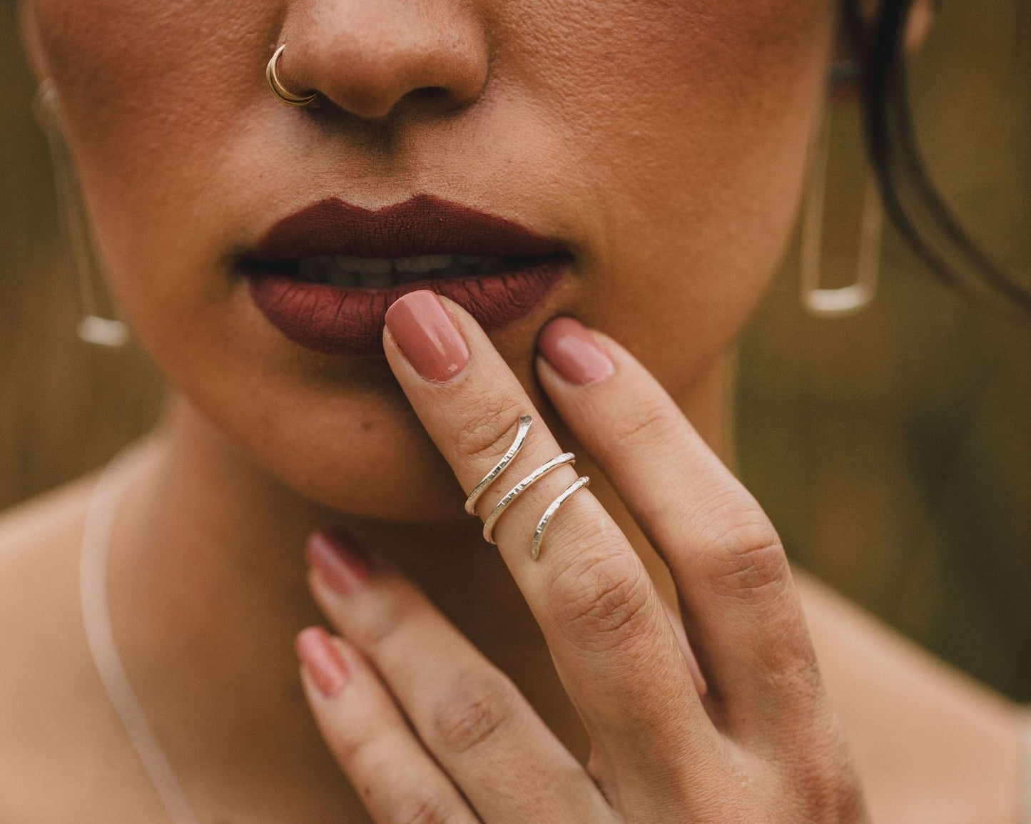 A close-up of a woman's face, focusing on her lips and fingers adorned with rings.