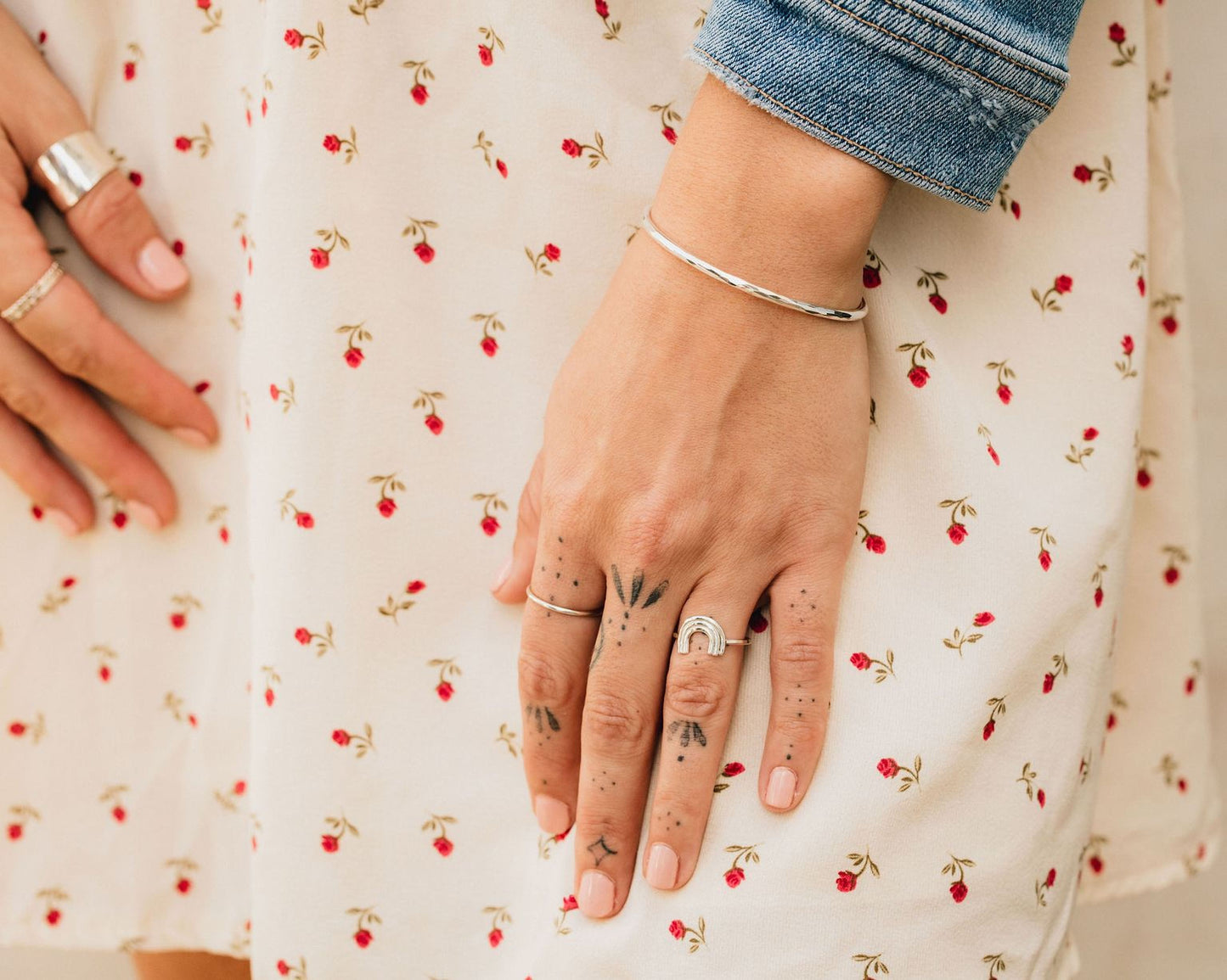 A close-up view of a person's hand wearing multiple rings and a bracelet, with a denim jacket visible in the background.