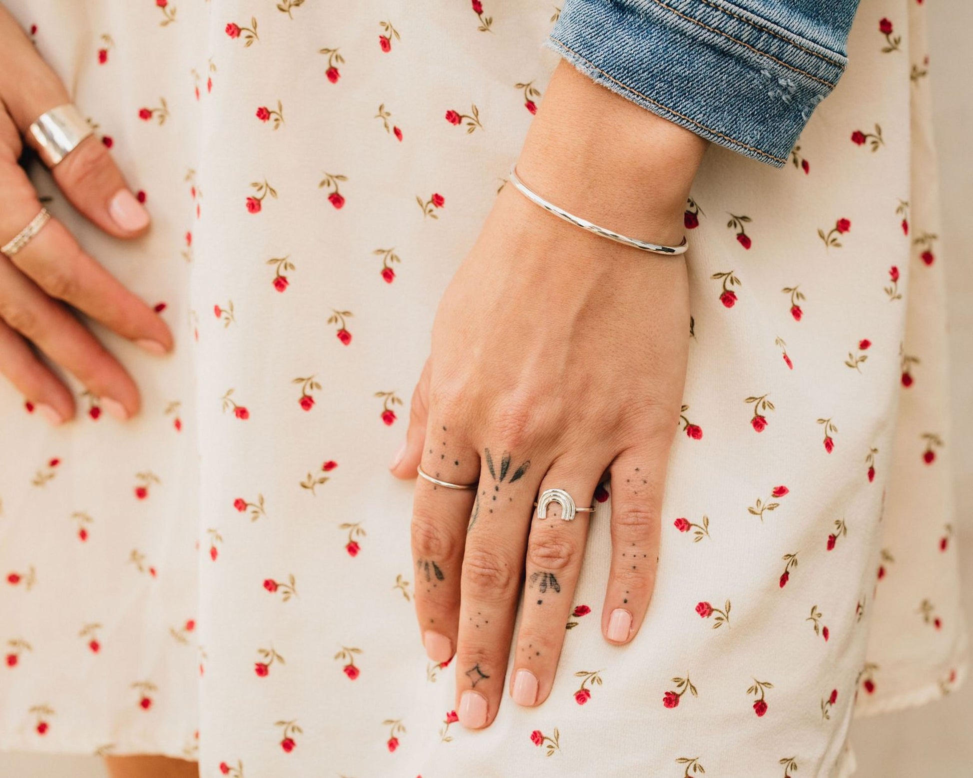A close-up view of a person's hand wearing multiple rings and a bracelet, with a denim jacket visible in the background.