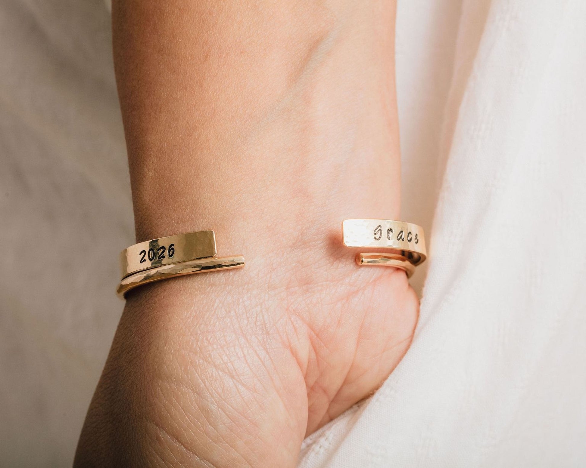 A gold-colored bracelet with two engraved tags on the wrist.