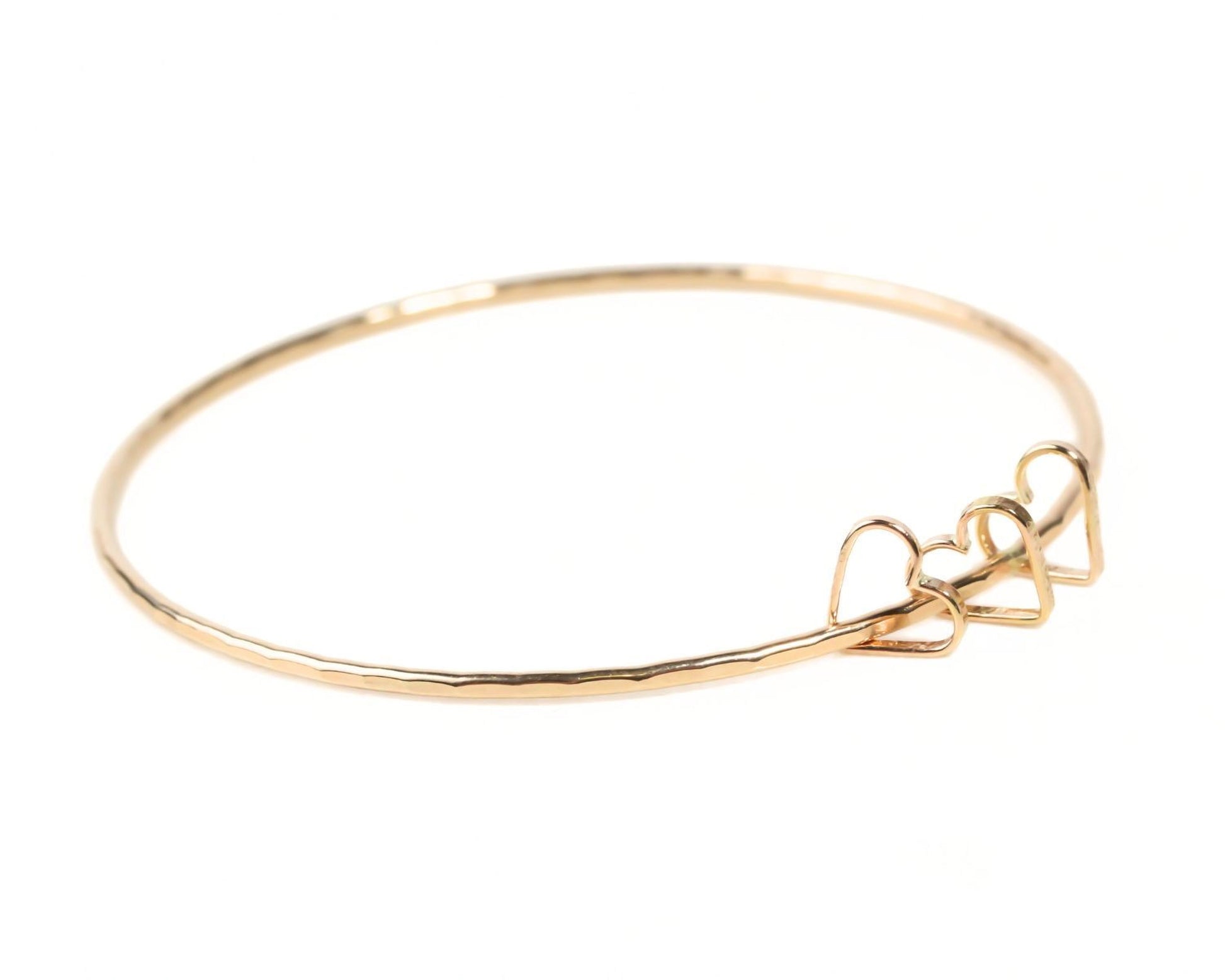 A gold-colored bangle bracelet with a heart-shaped clasp.