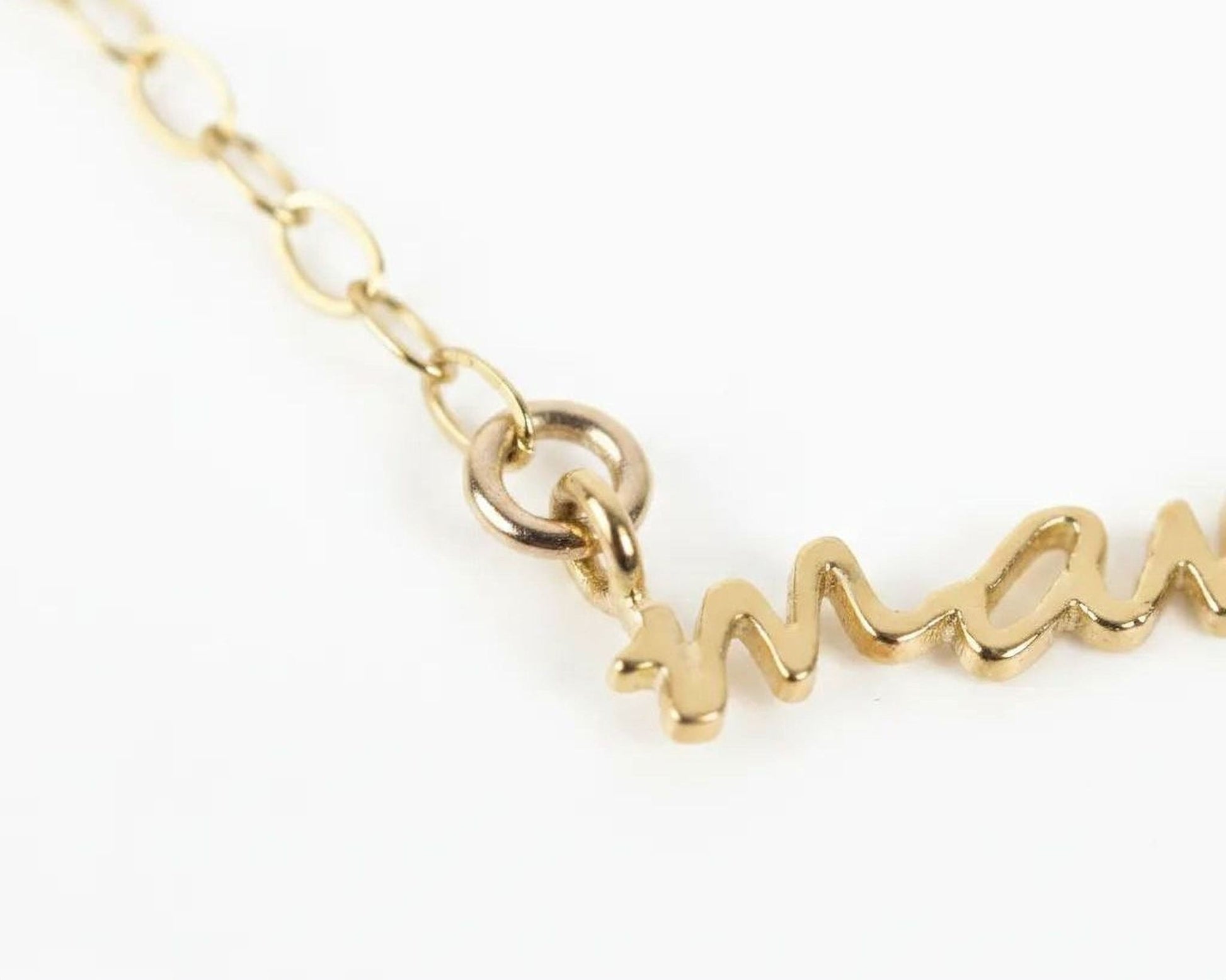 A close-up view of a gold-colored necklace with a chain and a charm in the shape of the word "Mama".