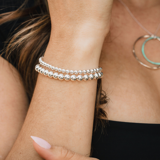 A close-up view of a person's wrist adorned with multiple silver-colored bracelets and a necklace.