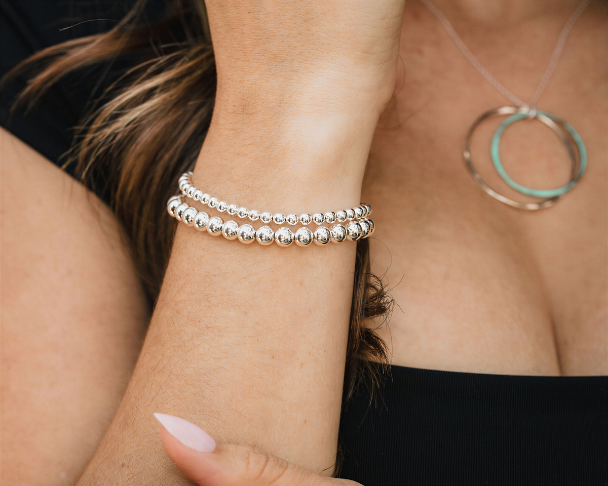 A close-up view of a person's wrist adorned with multiple silver-colored bracelets and a necklace.