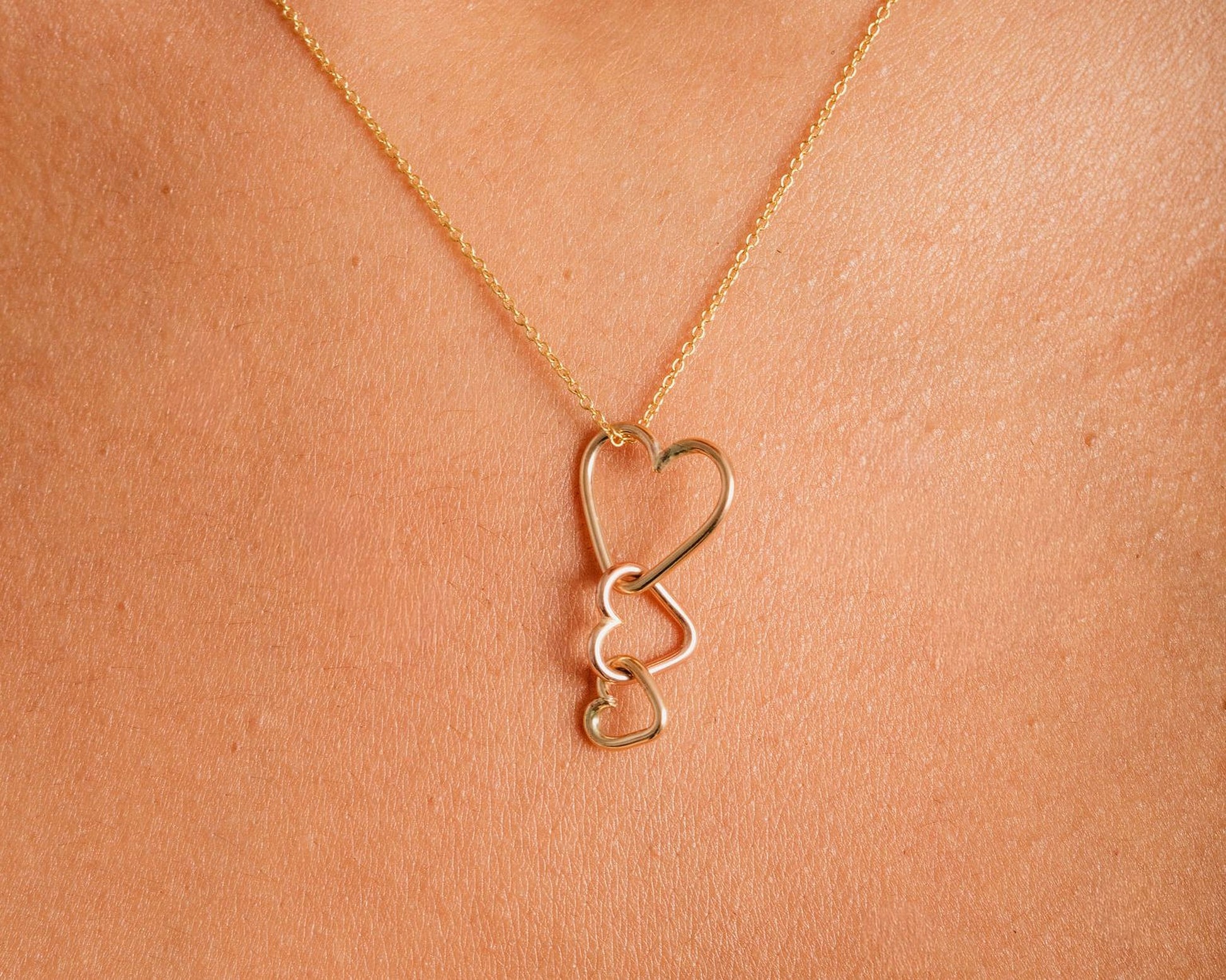 A close-up view of a gold necklace with a pendant featuring three interlocking heart shapes.