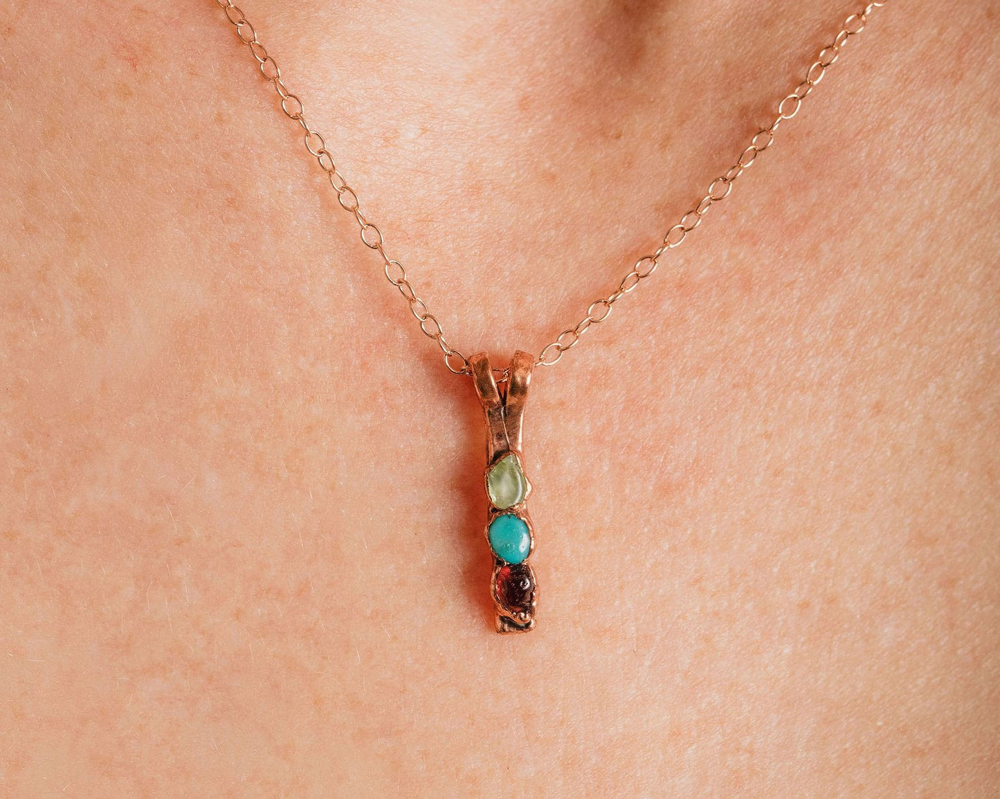 A close-up of a gold-colored necklace with a pendant featuring three colored stones.