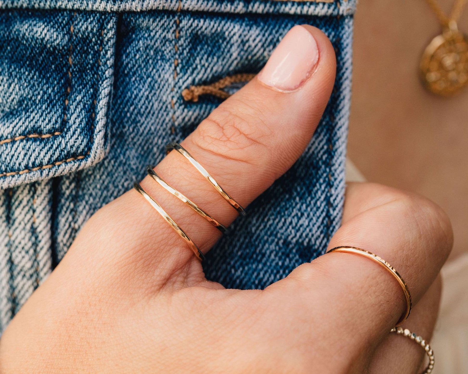 A close-up of a person's hand wearing three gold rings on the fingers.
