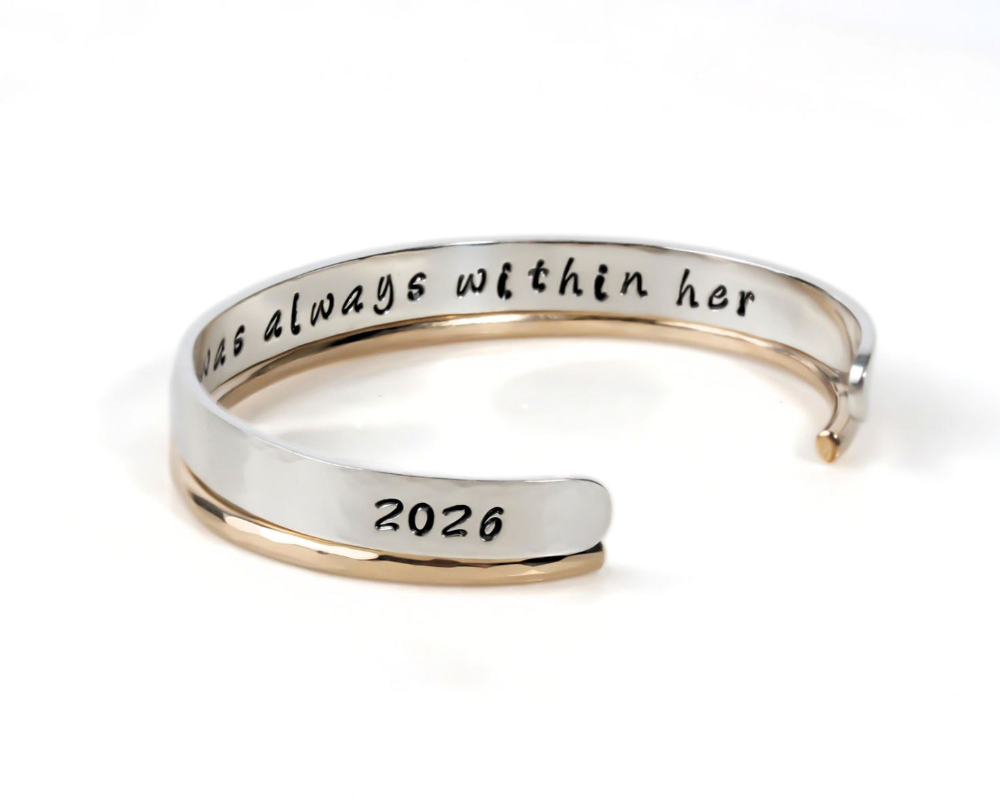 A silver and gold bracelet with the text "2026" engraved on it.