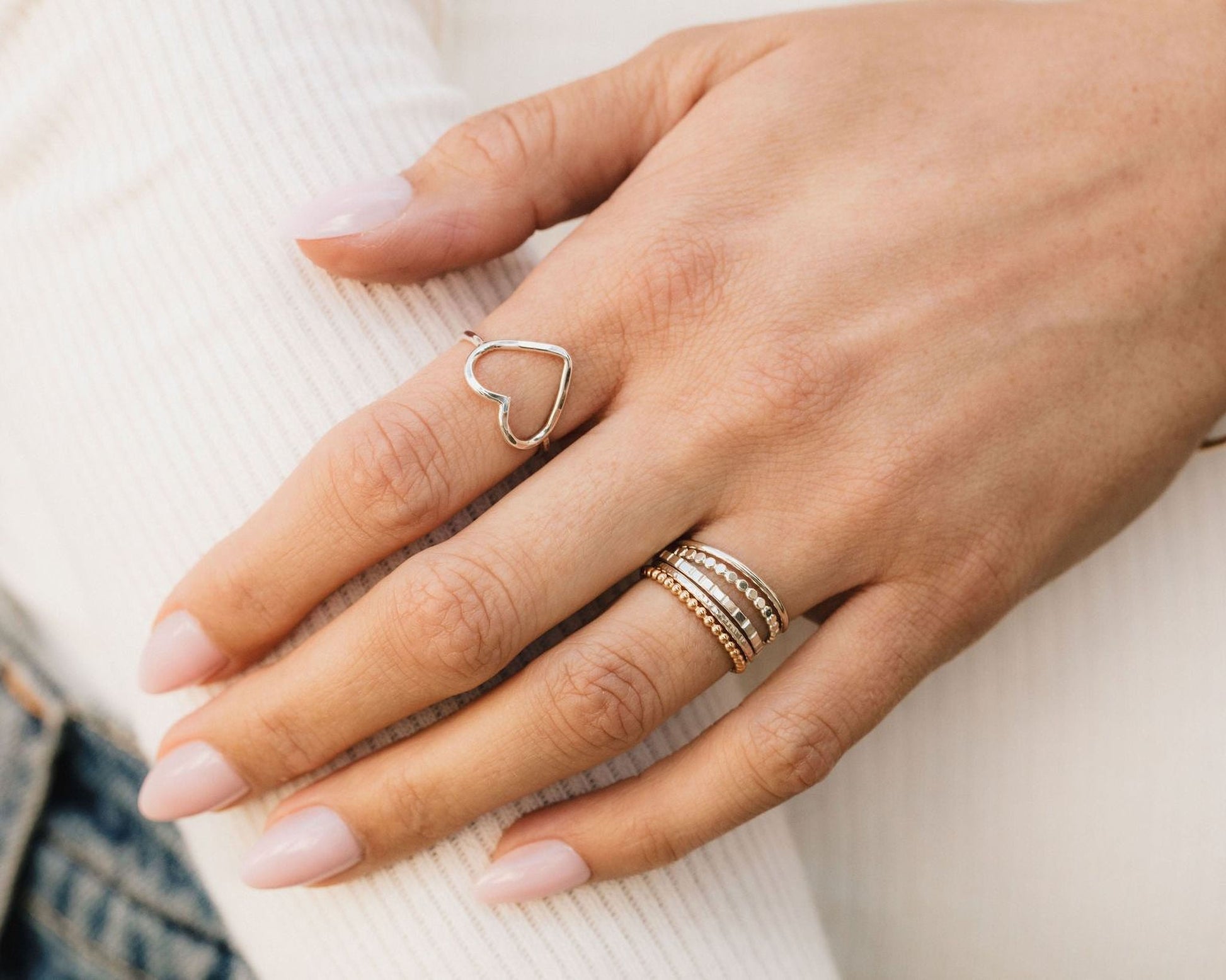 A close-up view of a person's hand wearing multiple rings, including a heart-shaped ring and a ring with multiple tiers.