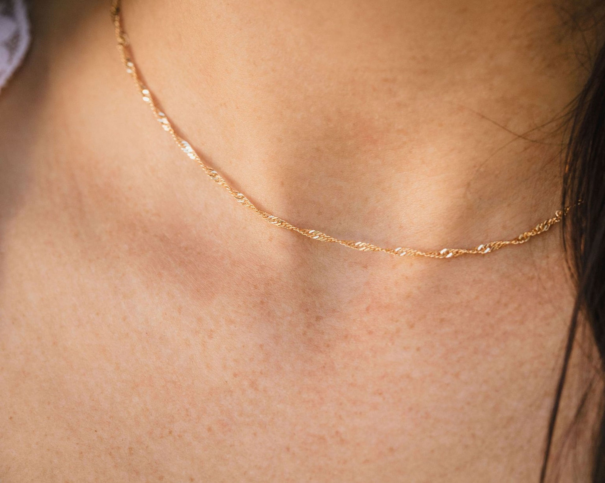 A close-up view of a delicate gold necklace with a twisted chain, worn around the neck of a person.