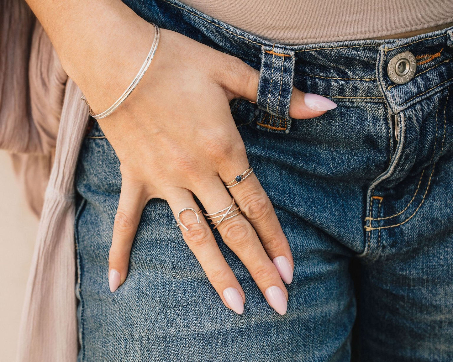 A close-up view of a person's hand wearing multiple rings on their fingers, with the hand resting on a pair of blue jeans.