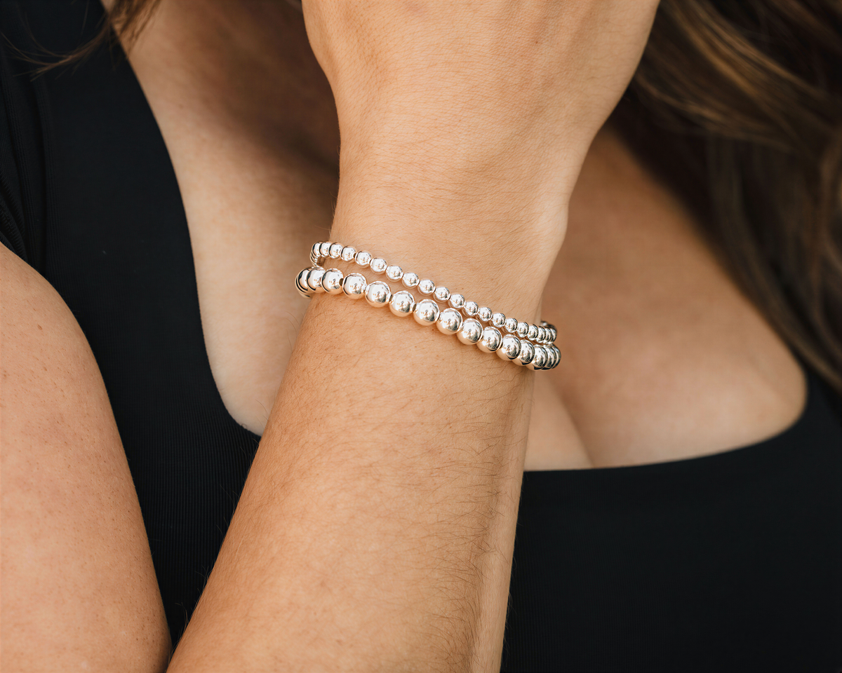 A close-up of a person's wrist wearing a bracelet with multiple silver beads.