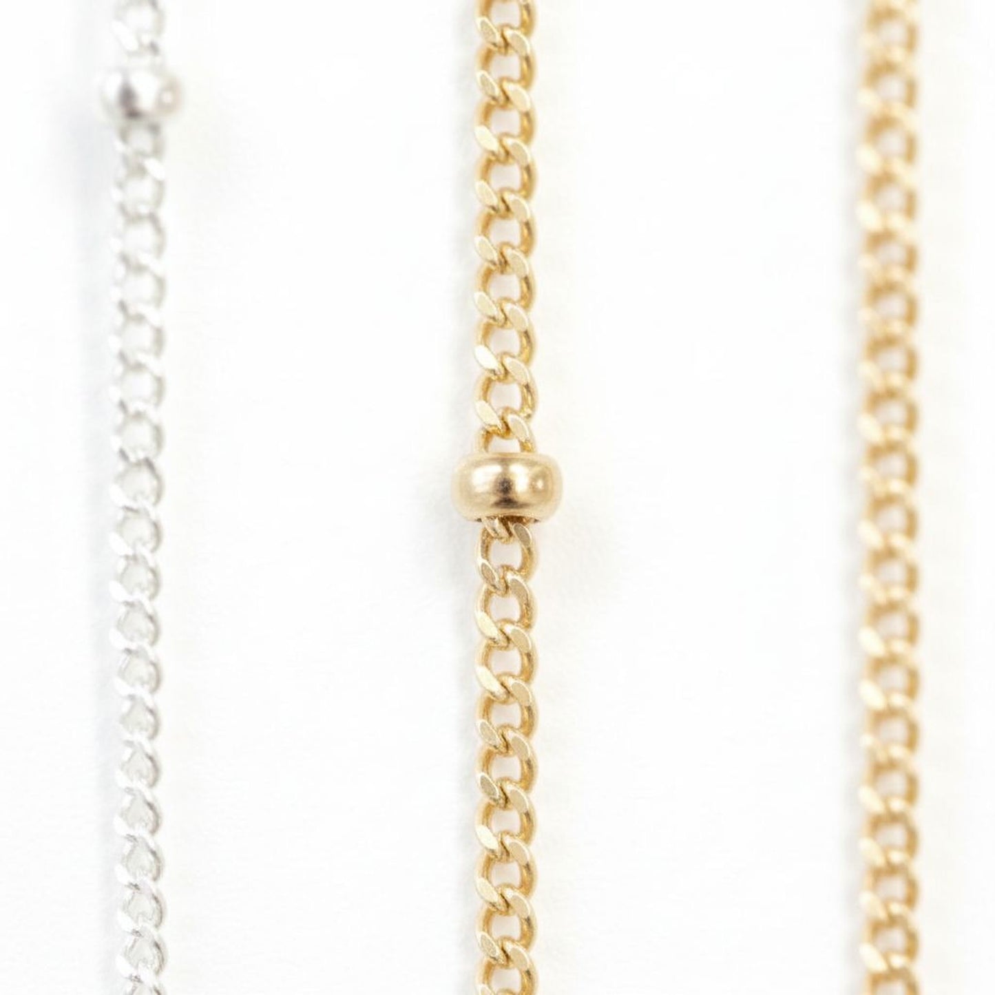 a close-up view of three different chain necklaces, each with a gold-colored metal chain and a small gold-colored bead at the center.