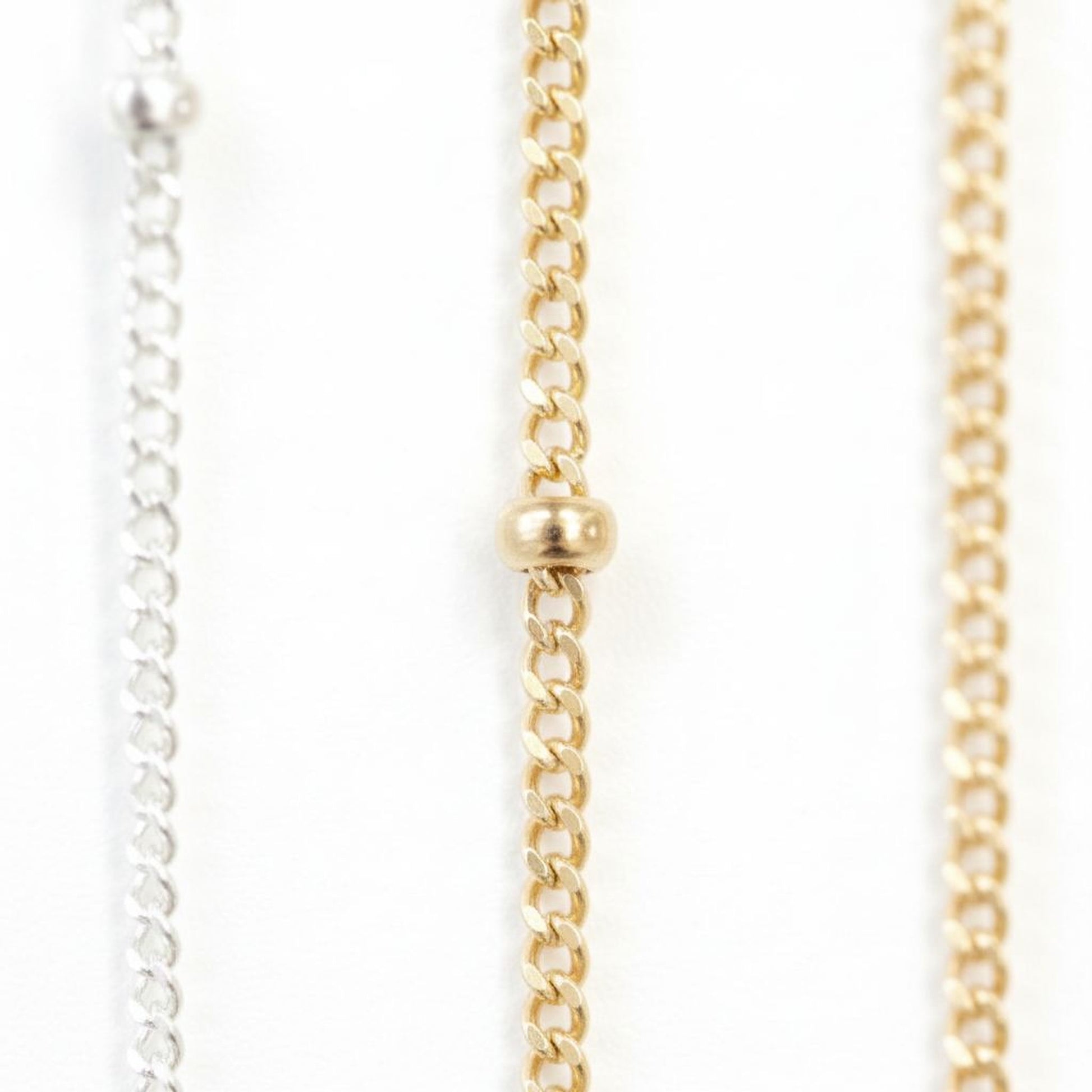 a close-up view of three different chain necklaces, each with a gold-colored metal chain and a small gold-colored bead at the center.
