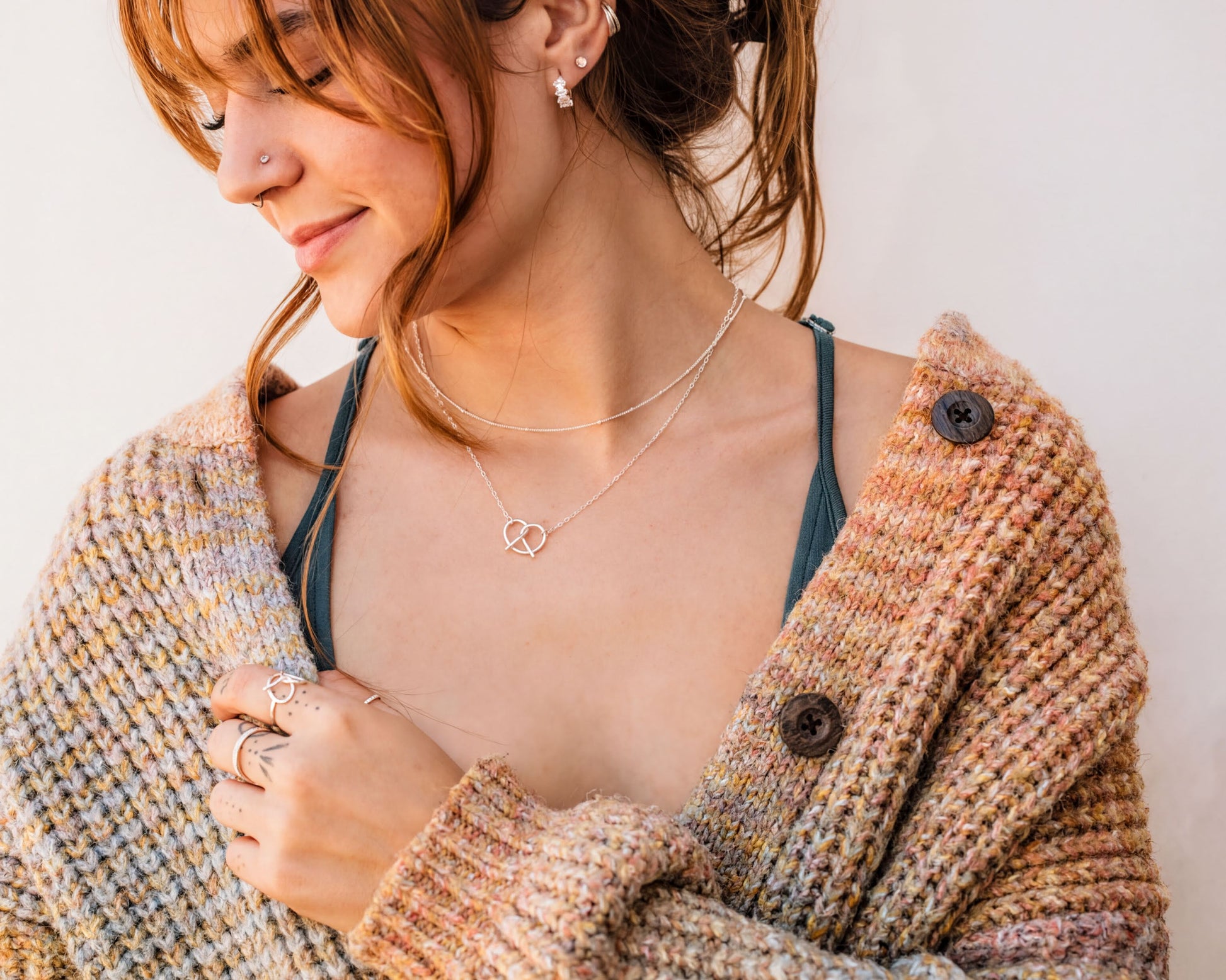 A woman with red hair wearing a brown cardigan and multiple rings on her fingers is smiling at the camera.