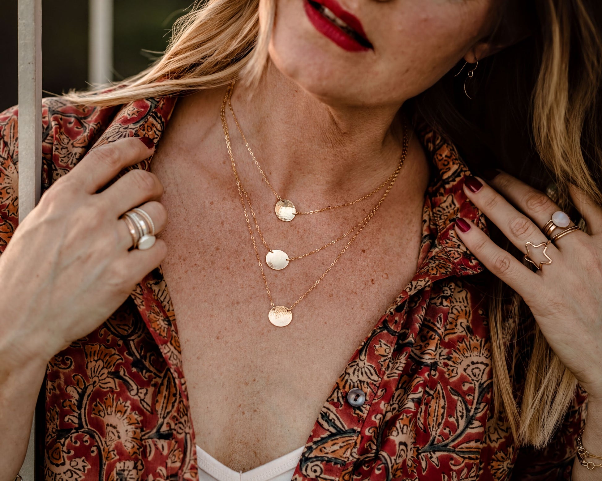 A close-up of a woman's neck and chest wearing multiple gold necklaces and rings.