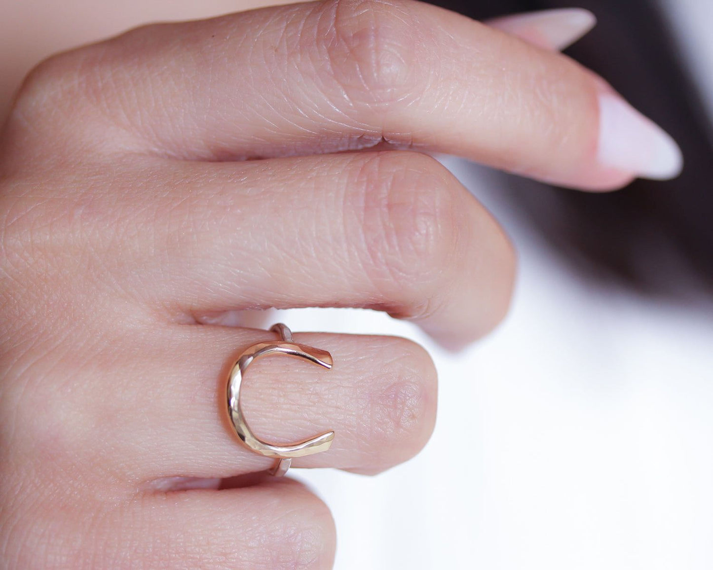A close-up of a person's hand wearing a gold ring with a letter 'C' on it.